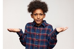 Handsome teen boy of black ethnicity dressed in flannel shirt standing against white background with questioning face expression, having no idea of what's going on, expressing confused feelings