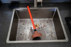 Overflowing kitchen sink, clogged drain. Plunger (force cup) in the sink. Plumbing problems.