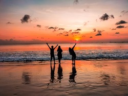 Silhouette of friends having fun on the Jimbaran beach, Bali, Indonesia, enjoying the atmosphere at sunset. Landscape panoramic photo against orange sky background with fresh summer concept