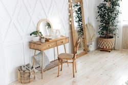 Wooden boudoir table with vintage chair. Full length mirror with wooden frame. Flowers in pots indoors. Wooden floor. Scandinavian style handmade wooden furniture. Boho style interior. Nobody