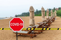 ''COVID-19'' road sign and a quarantine warning tape against loungers and folded beach umbrellas in a desolate tropical beach