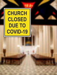 ''Church closed due to COVID-19'' information sign against a defocused church interior