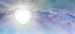 Rainbow heart light burst sky background - beautiful romantic ethereal cloudscape with a vibrant light burst on left side overlaid with a rainbow border heart and white centre for messages
