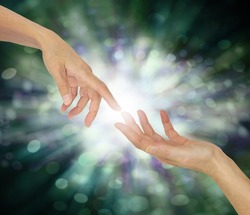 Receiving a Reiki attunement concept - one hand touching another hand with white light between against an ethereal graduated green bokeh magical  background with copy space for text
