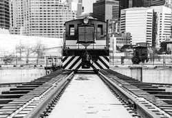 Front view of an old locomotive that stands on the rails within the metropolis. Black and white photo