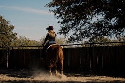 Cowgirl riding horse in dirt outdoor arena for western lifestyle.