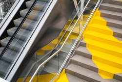 Stairs or escalator? Yellow stairs parallel to the escalator. The easy way or the hard way? Climbing stairs for weight loss and exercise 