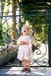 Little girl with soft toy yawns near garden patio gate