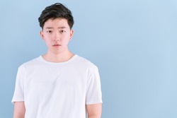 Young Asian casual teenage boy indicate blank space on light blue background.