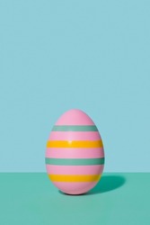 Pink striped Easter egg in 80s-90s retro style. A pink egg with multi-colored stripes on a two-tone background of mint and blue hues. Happy Easter vintage card.