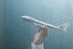 Businessman holding airplane behind wet window