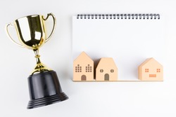 Top view of Blank notebook white paper, paper house model and Golden trophy isolated on white background with space for your message.Concept winner
