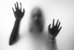 Horror woman behind the matte glass in black and white. Blurry hand and body figure abstraction.Halloween background