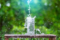Drink water pouring in to glass over sunlight and natural green background.Water splash  in glass Select focus blurred background.
