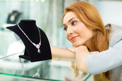 Young happy beautiful woman looking at the luxurious diamond necklace smiling joyfully shopping at the jewelry store copyspace affordable dreaming consumerism happiness emotions lifestyle retail.