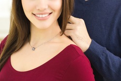 Perfect details. Cropped close up of a beautiful woman smiling happily while her man is wearing a necklace around her neck love romance passion affection anniversary gift present valentine's luxury 