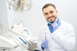 Professional male dentist smiling to the camera holding dental instruments sitting at his office copyspace dentistry profession doctor treatment curing help helpful skilled job worker health medical