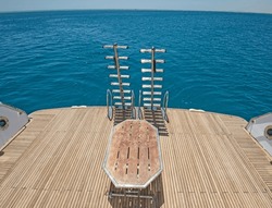 Metal steel ladders on back teak wooden deck of a large luxury motor yacht sailing on a tropical ocean