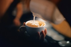 Professional barista pouring latte foame over coffee, espresso and creating a perfect cappuccino
