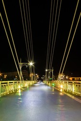 Perspective view of illuminated span of the Bridge of Lovers with people blurred in motion at night, Tyumen, Russia