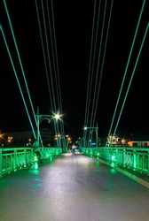 Perspective view of illuminated span of the Bridge of Lovers with people blurred in motion at night, Tyumen, Russia