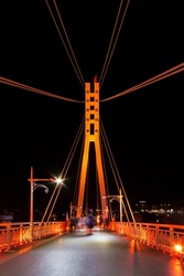Perspective view of illuminated span and pylon of the Bridge of Lovers with people blurred in motion at night, Tyumen, Russia