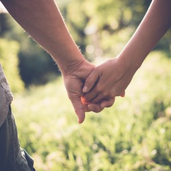Young couple in love walking in the summer park holding hands, filtered image