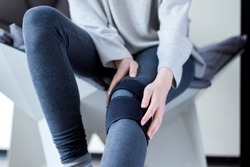 Closeup female leg in grey leggings dressed in knee brace to help promote recovery of bones, muscles, ligaments. Woman is feeling pain in joints after injury. Arthritis and meniscus diseases concept.