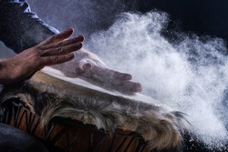 Man is playing on djembe drum, covered with talcum powder. Flour splashes on dark background. Summer festival concert performance. Ethnic rhythm. Percussion musical instruments and culture concept. 