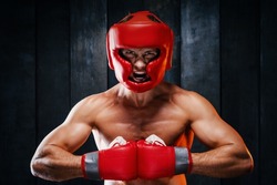 Dynamic motion portrait of sportive muscular athletic man in boxer gloves, helmet and shorts practicing attack. Fit strength male fighter kickboxing engaged in gym with screaming face in movement.