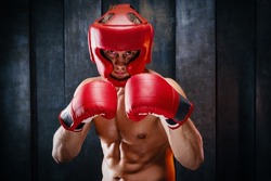 Dynamic motion portrait of sportive muscular athletic man in boxer gloves, helmet and shorts practicing attack. Fit strength male fighter in movement engaged in training gym, in a fight without rules.