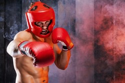 Dynamic motion portrait of sportive muscular athletic man in boxer gloves, helmet and shorts practicing attack. Fit strength male fighter kickboxing engaged in gym with screaming face in movement.