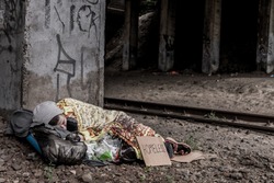 Homeless woman with sign sleeping under the bridge near the rail track