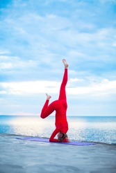 female in a red yoga makes yoga asana in sun rays near a sea