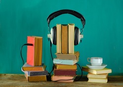 audio book concept with stack of books and vintage headphone on teal background, good copy space.
