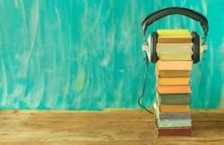 audio book concept with stack of books and vintage headphones on teal background, large copy space.
