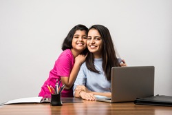 Working Indian mom works from home office with kid in pandemic. Woman and cute child using laptop. Freelancer workplace in cozy home. Happy mother and daughter.