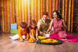 Indian family lighting or arranging oil lamp or diya around flower rangoli on diwali festival night