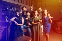 Group of indian asian friends sitting at lounge bar, having drinks or cocktails, celebrating new year, birthday or success