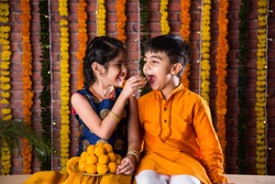 Indian kids, little brother and sister celebrating Diwali, Raksha Bandhan, Bhai Dooj with big gift box and sweet laddoo