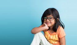 Cute little Indian girl with spectacles smiling and posing for photoshoot, against sky blue background