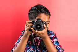 10 year old indian boy holding digital camera or DSLR over red background
