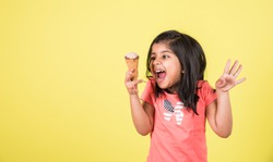 Indian/Asian cute little girl eating Ice cream in cone or mango bar/candy. Isolated over colourful background