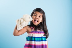 cute little indian girl playing with white soft toy puppet with happy expressions. Standing against sky blue background