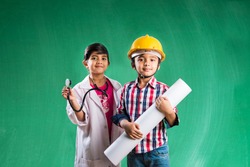Kids and education concept - Small indian boy and girl posing in front of Green chalk board in engineers fancy dress and doctor costume with stethoscope