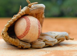 An old leather baseball mitt, or glove with a worn baseball laying on a home plate. There is clay around. Home plate needs to be dusted off. Shallow depth of field. Horizontal composition. Copy space