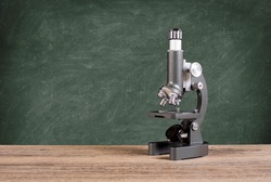 old microscope in front of the blackboard