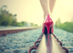 Female legs in red high heels on the rail of the railway. (Vintage style)