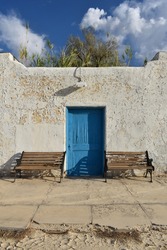 Old peeling paint wall with a blue door and two empty benches, vintage rustic background