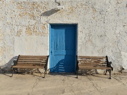 Old peeling paint wall with a blue door and two empty benches, vintage rustic background